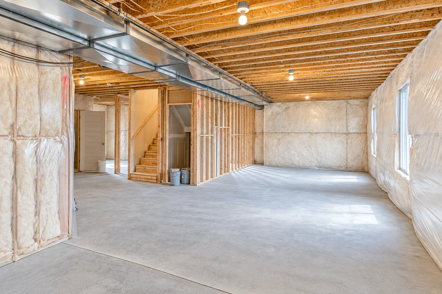 Basement walls are insulated between studs and covered with white facing, with exposed ceiling joists and a concrete floor.