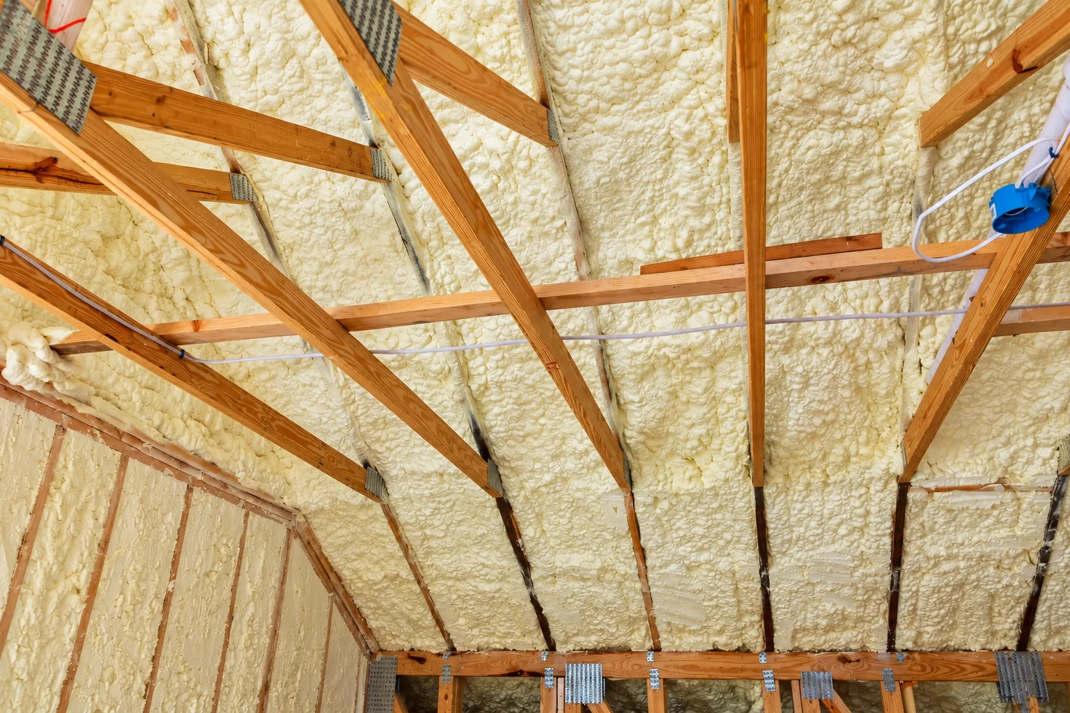 Spray foam insulation fills the roof and wall cavities of a wood-framed home interior.