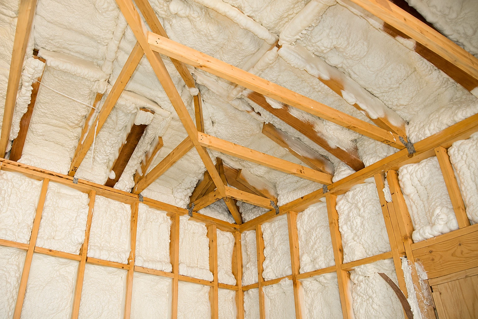 Open-cell spray foam fills the roof and wall cavities between exposed wooden framing.